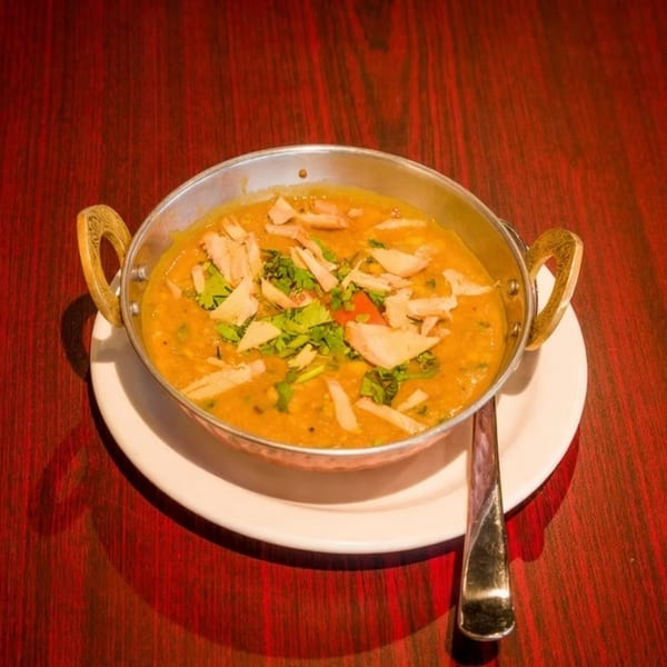 A metal bowl of yellow lentil soup with cilantro and flatbread pieces on a red wooden table.